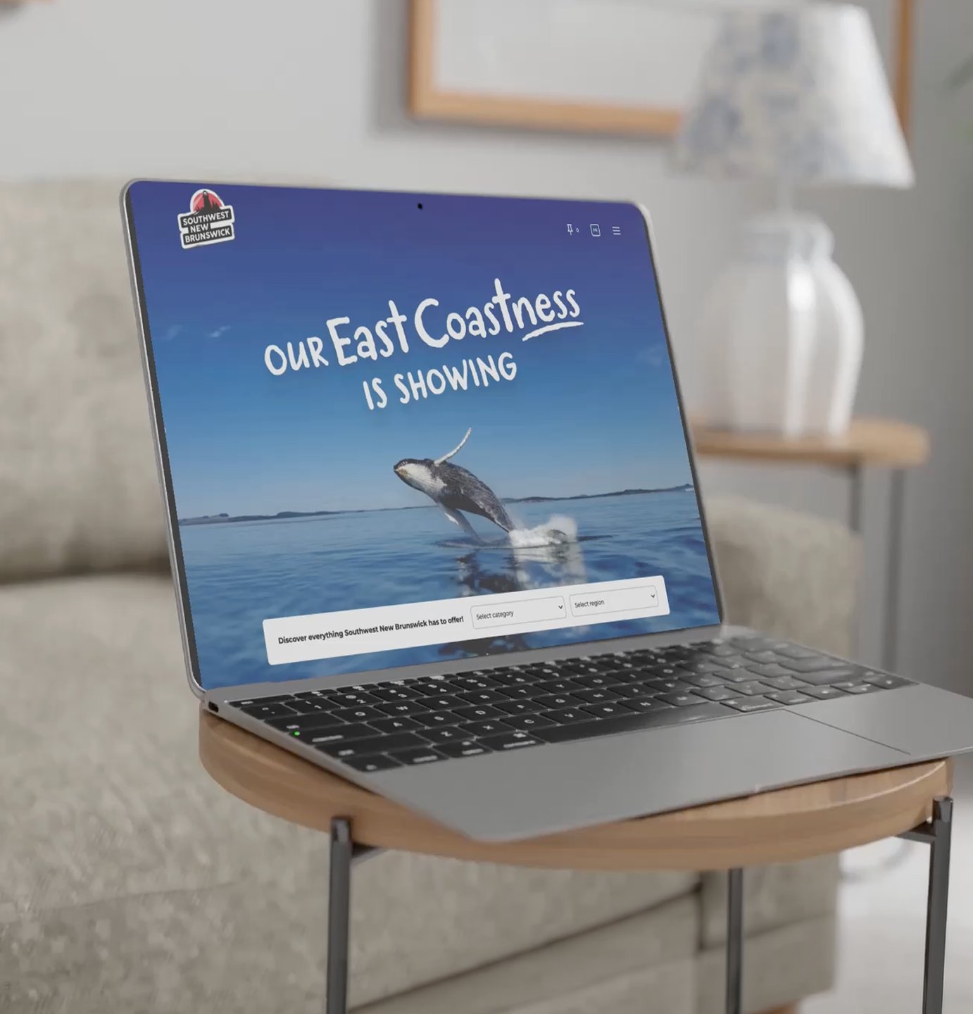 A laptop on a side table showing the 'Our East Coastness is showing' website with a breaching whale