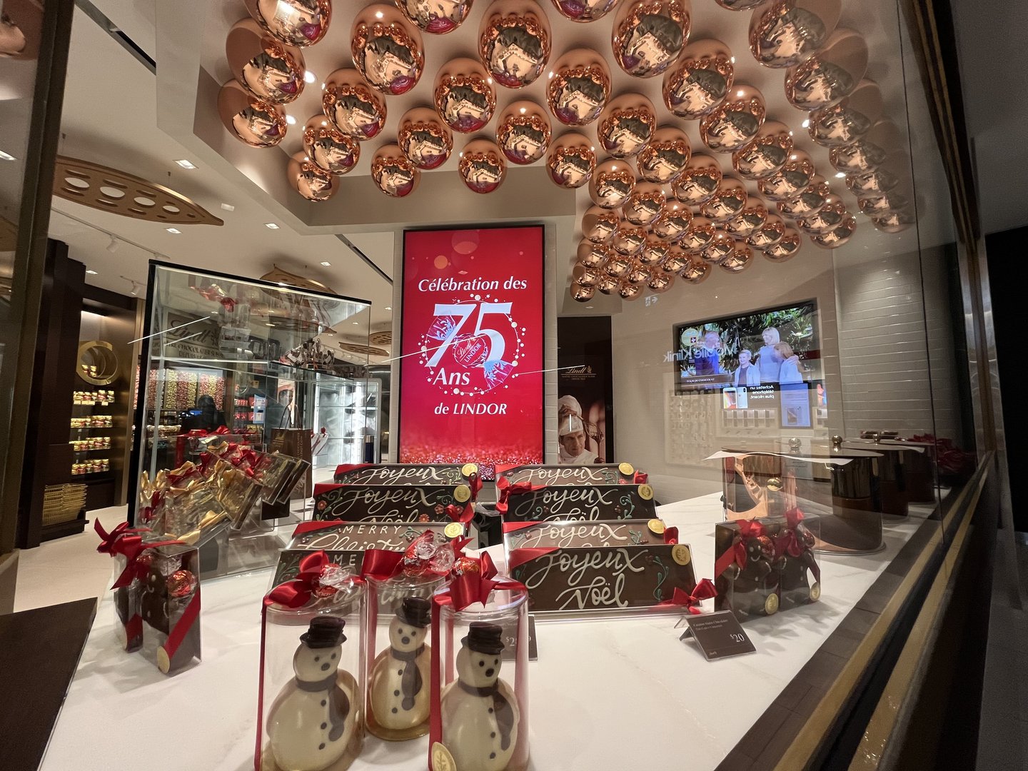 A ceiling of copper pots in the Lindt store's gifting zone, above seasonal chocolate figures and a Lindor 75th anniversary display