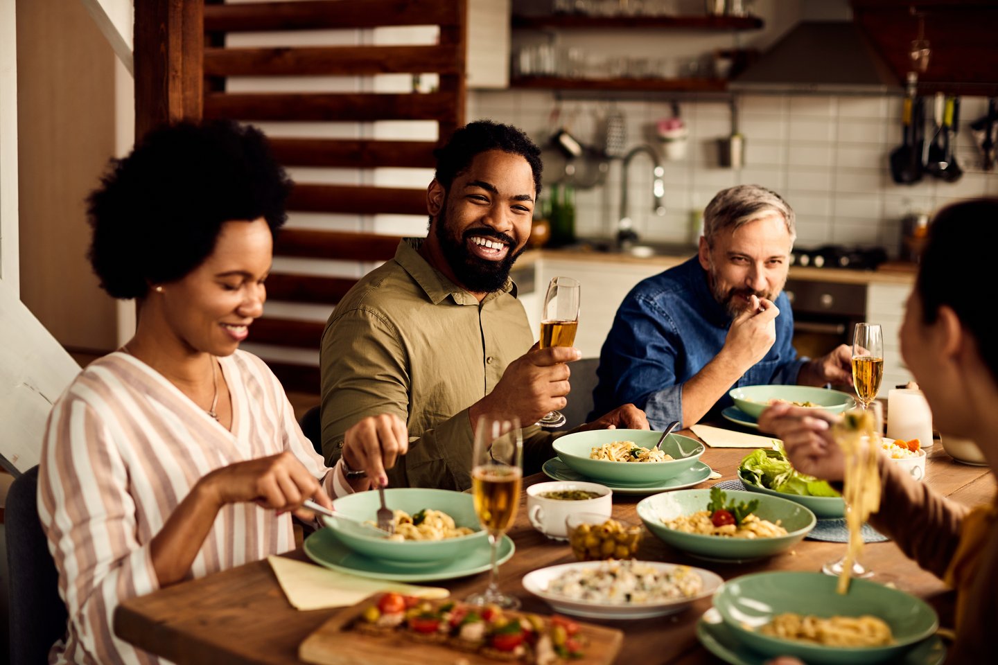 Friends laughing over dinner and glasses of wine at a kitchen table
