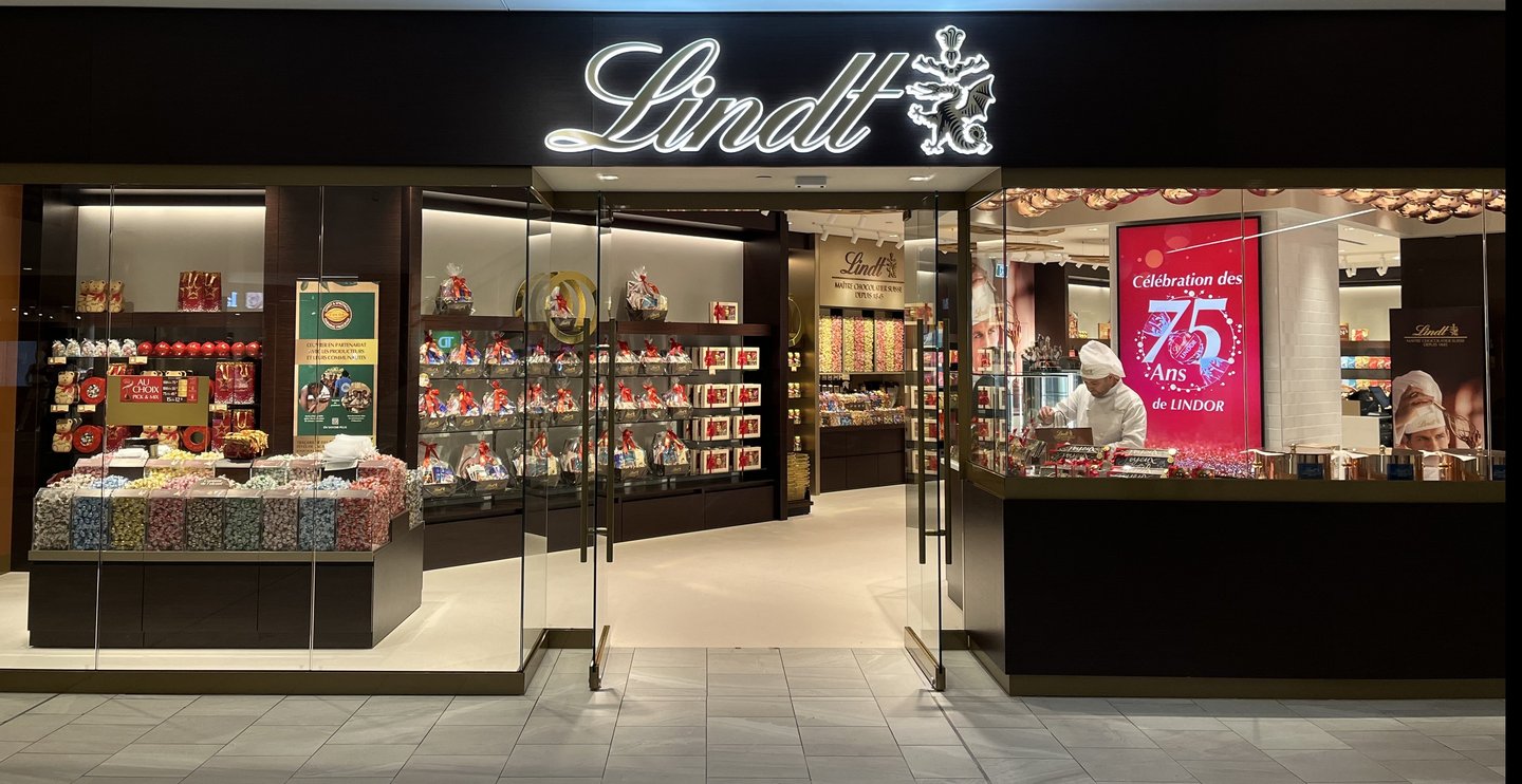 The Lindt flagship storefront at the Montreal Eaton Centre, with the illuminated Lindt sign, glass front and a Lindor 75th anniversary poster