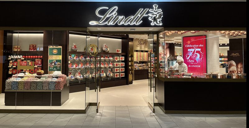 The Lindt flagship storefront at the Montreal Eaton Centre, with the illuminated Lindt sign, glass front and a Lindor 75th anniversary poster