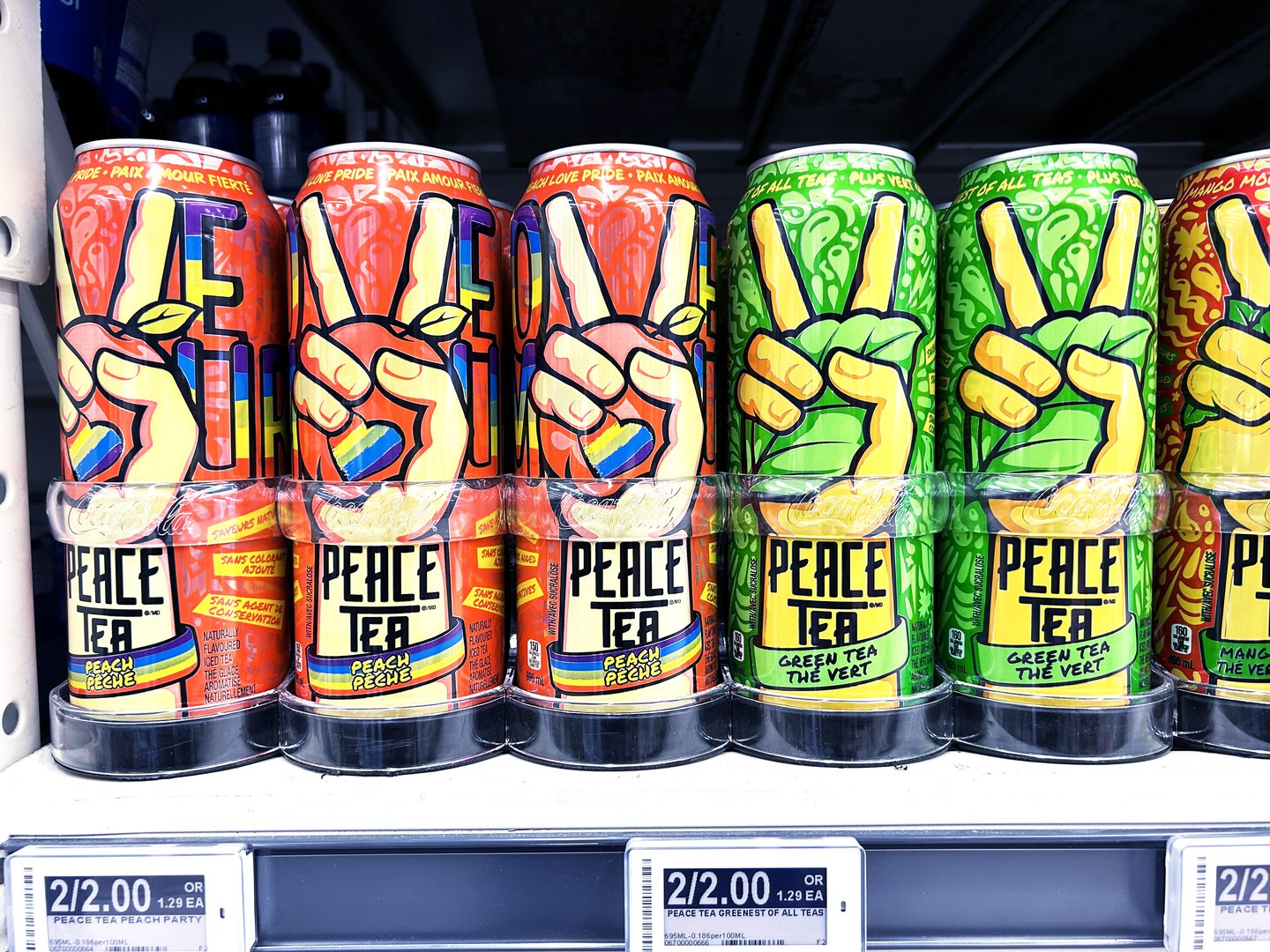 A store shelf of Peace Tea cans, peach and green tea flavours, each with the peace-sign hand and a rainbow band