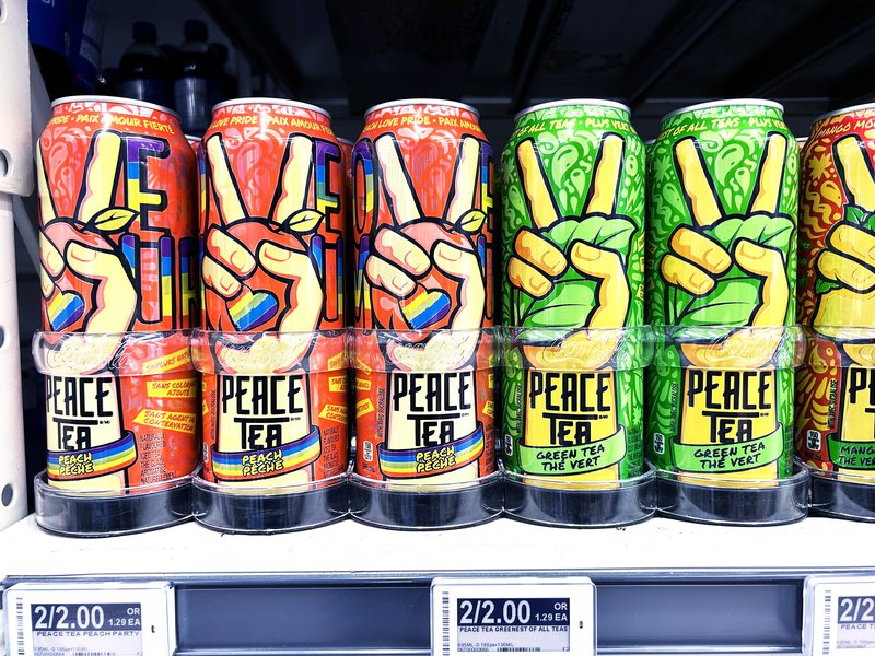 A store shelf of Peace Tea cans, peach and green tea flavours, each with the peace-sign hand and a rainbow band