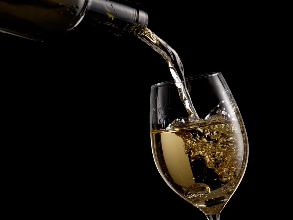 White wine pouring into a glass against a black background