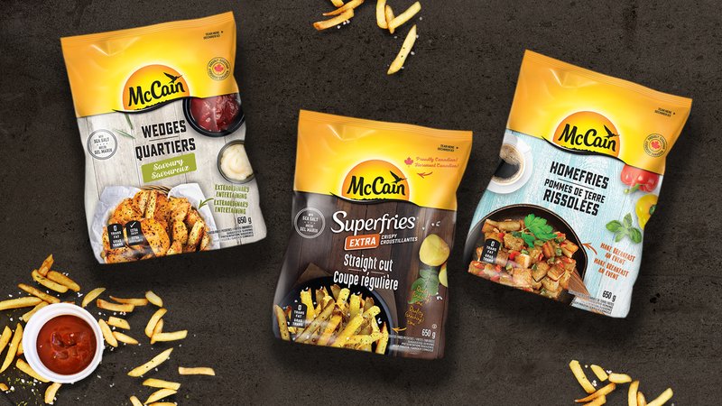 Three McCain frozen potato bags, Wedges, Superfries Straight Cut and Homefries, on a dark surface with scattered fries and ketchup