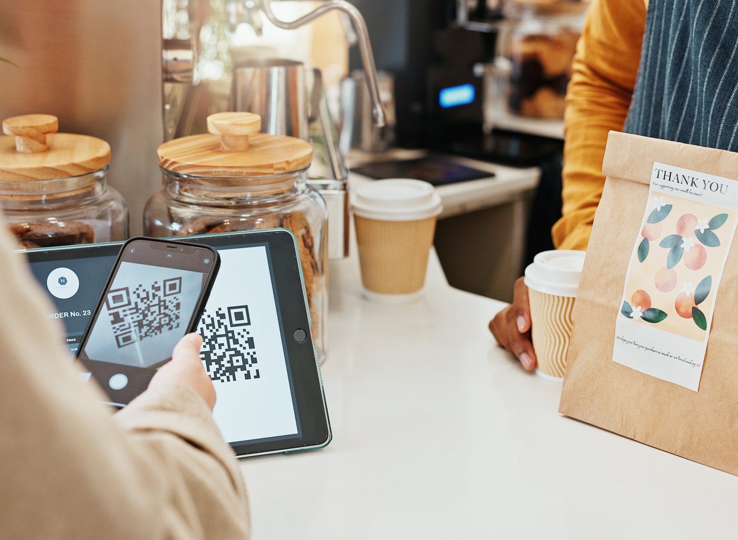 A phone scans a QR code to pay at a coffee shop counter