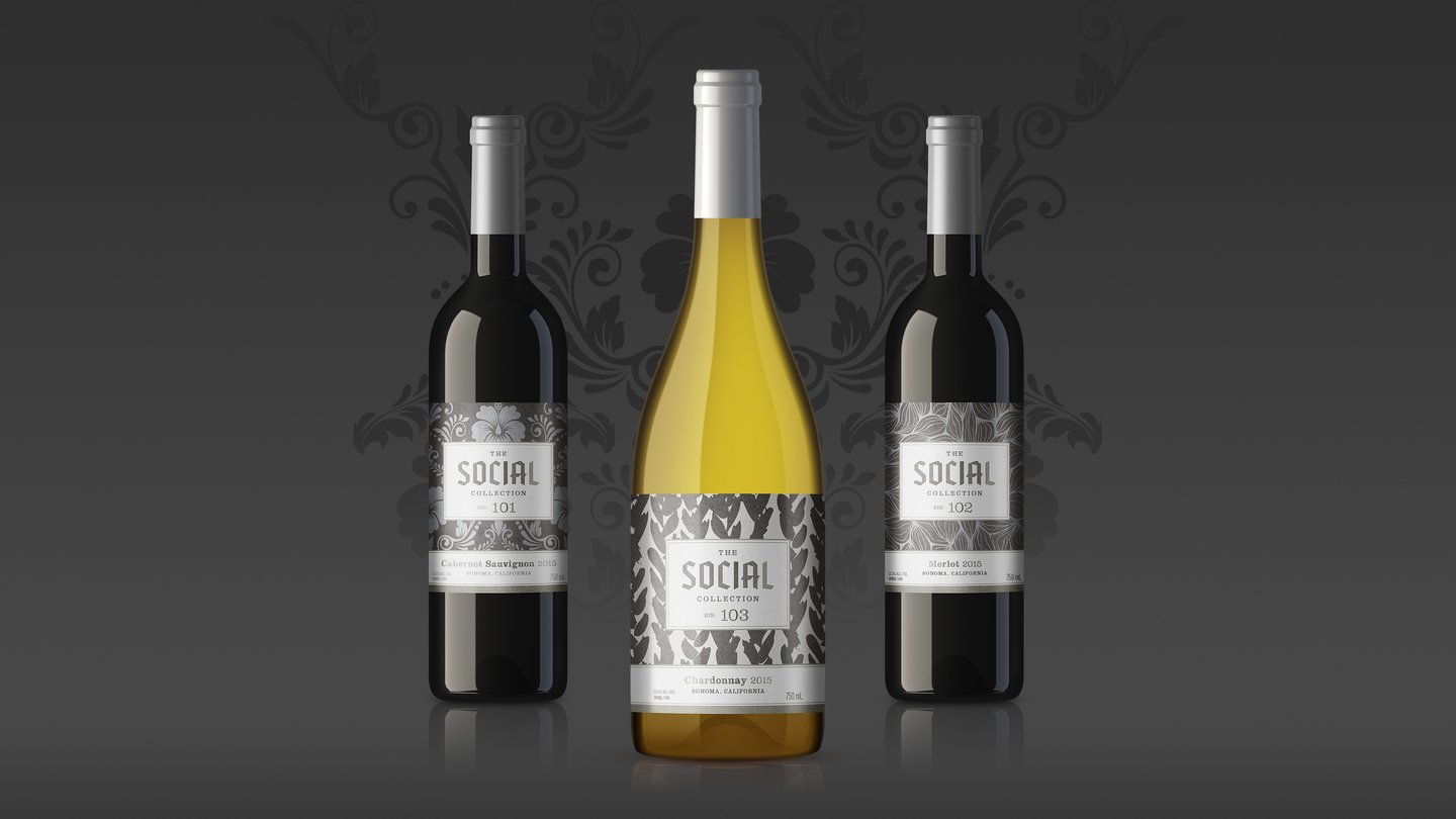 Three bottles of The Social Collection: two reds and a white, each with a different patterned label, on dark grey