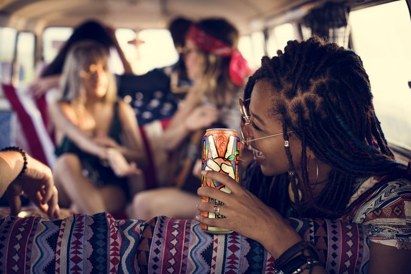 A woman with a rainbow wristband sips a Peace Tea can among friends in the back of a van