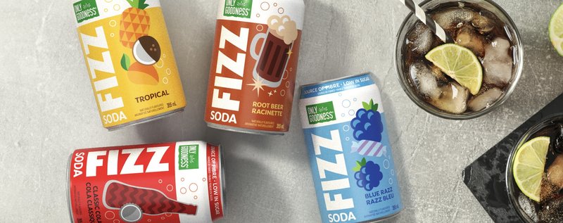 Only Goodness Fizz soda cans in tropical, root beer, classic cola and blue razz flavours on a stone counter with glasses of ice and lime