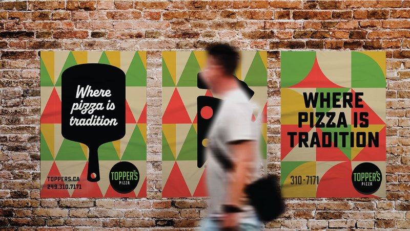Three Topper's 'Where pizza is tradition' posters on a brick wall, as a man walks past