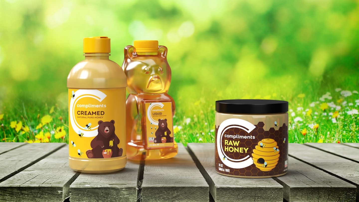 Compliments creamed honey, a honey bear squeeze bottle and a raw honey jar on a table in a sunny meadow