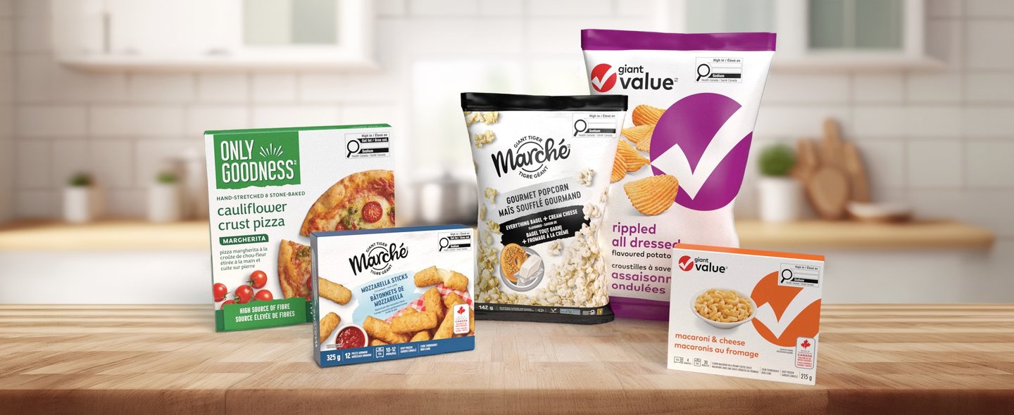 Grocery private brand packs on a kitchen counter: Only Goodness cauliflower crust pizza, Marche gourmet popcorn and Plant Value rippled chips and mac & cheese