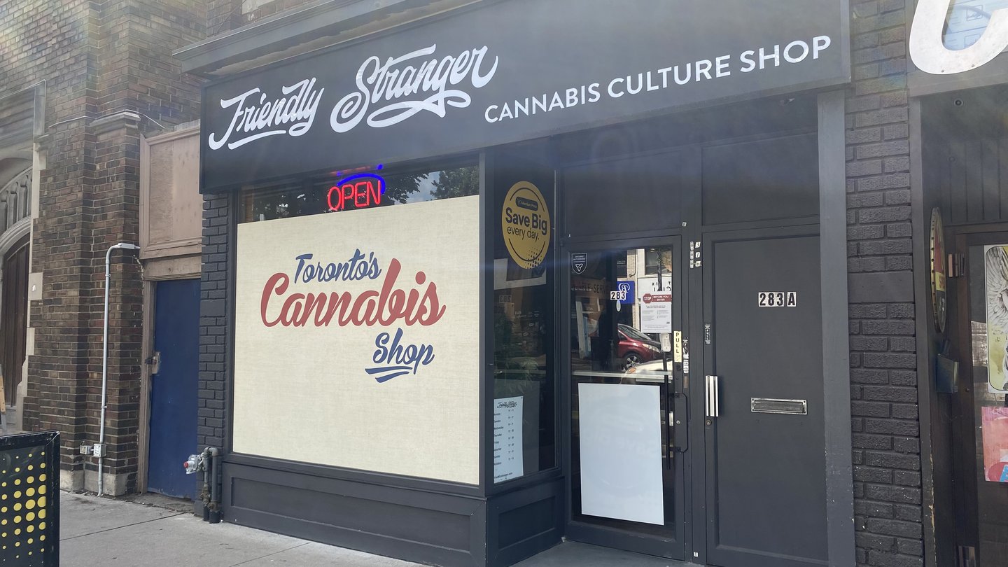 The Friendly Stranger storefront on a Toronto street, with the script logo on a black fascia and a 'Toronto's Cannabis Shop' window graphic