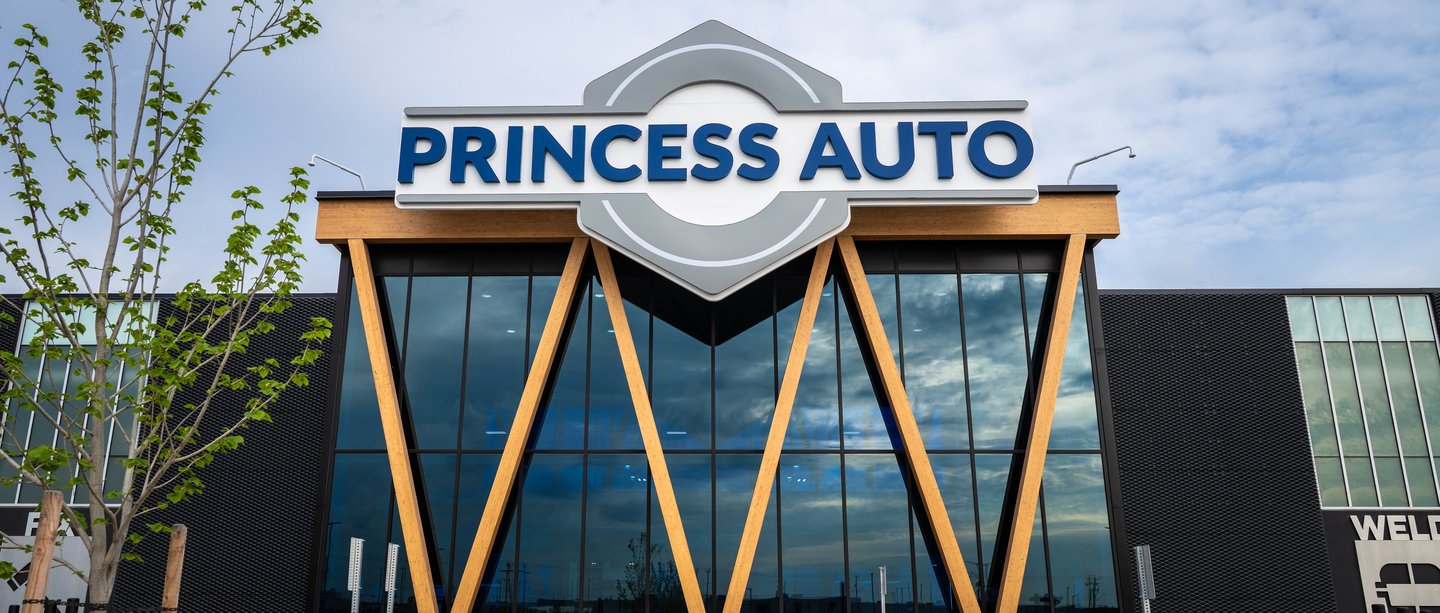 The Princess Auto flagship storefront at dusk: the hexagonal sign above a glass facade framed by angled wood beams