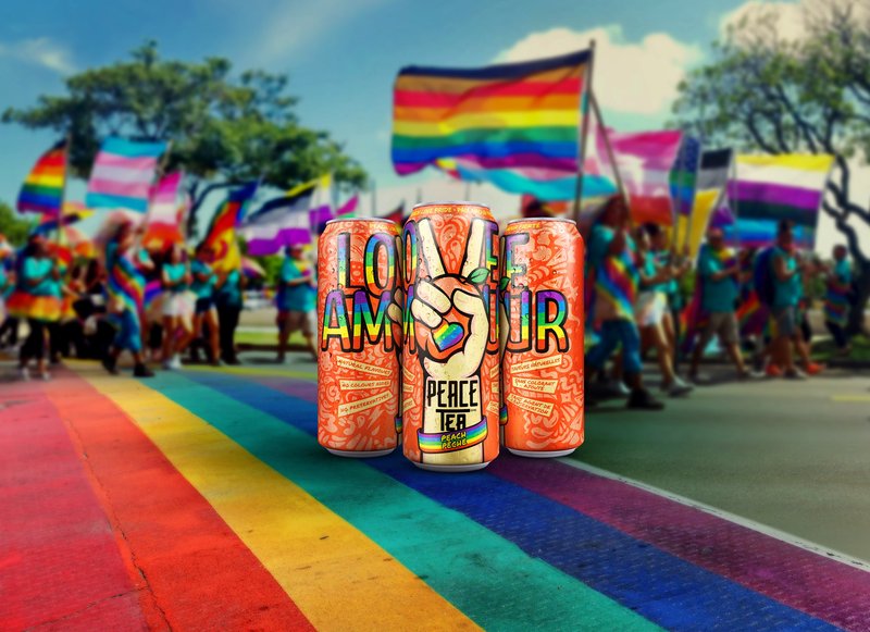 Three Peace Tea cans spelling 'Love' and 'Amour' with peace-sign hands, standing on a rainbow crosswalk at a Pride parade