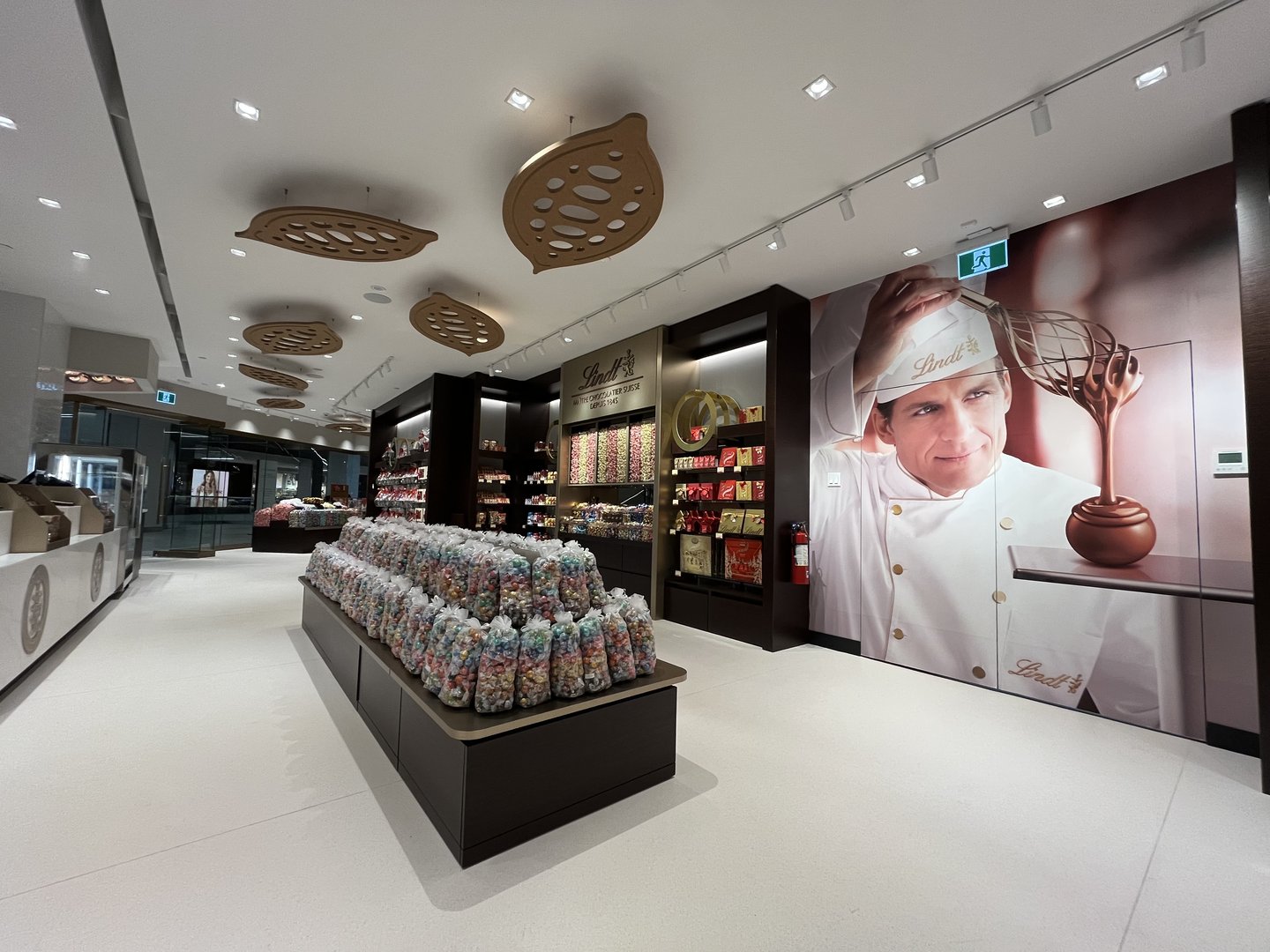 The redesigned Lindt store's cash area, with open floor around the Pick & Mix island and the chocolatier mural
