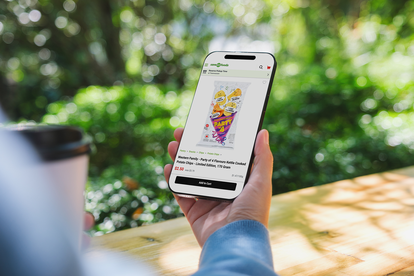 A hand holds a phone showing the Party of 4 kettle chips product page in the Save-On-Foods app