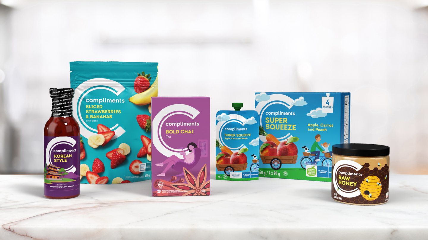 A line-up of redesigned Compliments products on a marble counter: Korean style sauce, sliced strawberries and bananas, bold chai tea, apple super squeeze pouches and raw honey