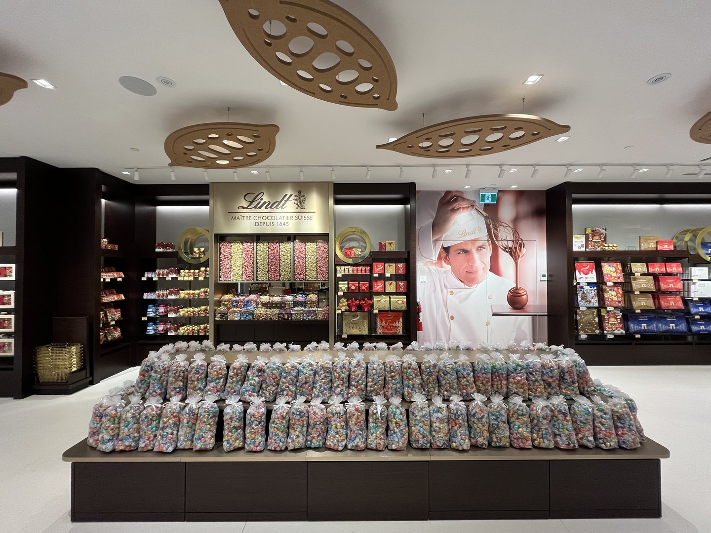 The redesigned Lindt store's open layout: a central Pick & Mix island of Lindor truffles in front of a portrait of the maitre chocolatier