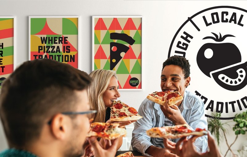 Friends eating pizza slices under Topper's 'Where pizza is tradition' posters and the Dough Local Sauce Tradition stamp