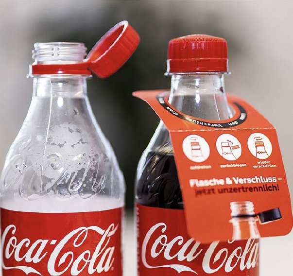 Two Coca-Cola bottles with tethered caps and a German tag reading 'bottle and cap, now inseparable'