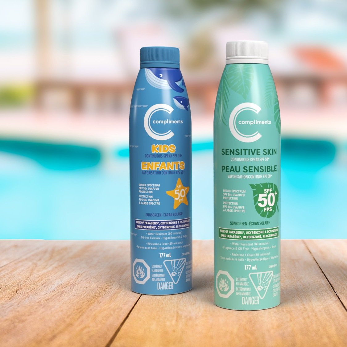 Compliments Kids and Sensitive Skin SPF 50 sunscreen sprays on a wooden table beside a pool