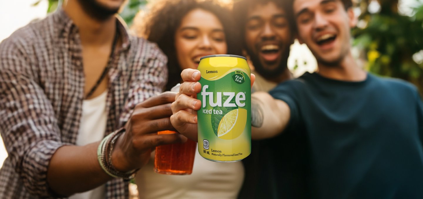 Four friends laughing and raising cans of Fuze iced tea together outdoors