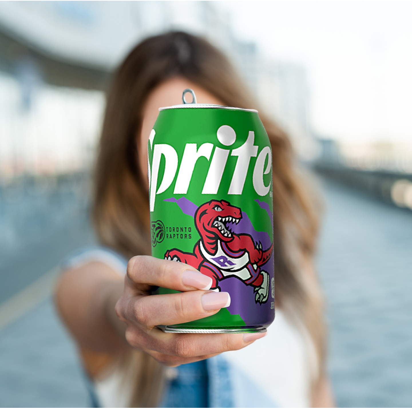 A woman holds the Sprite Toronto Raptors can out toward the camera on a city waterfront