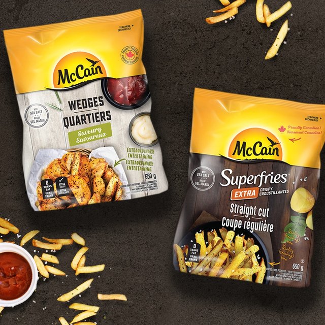 McCain Wedges and Superfries Extra Crispy Straight Cut bags on a dark surface with scattered fries and a dish of ketchup