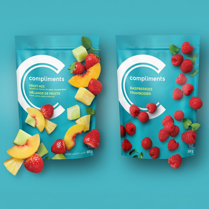 Two Compliments frozen fruit bags, Fruit Mix and Raspberries, on a teal background with scattered fruit