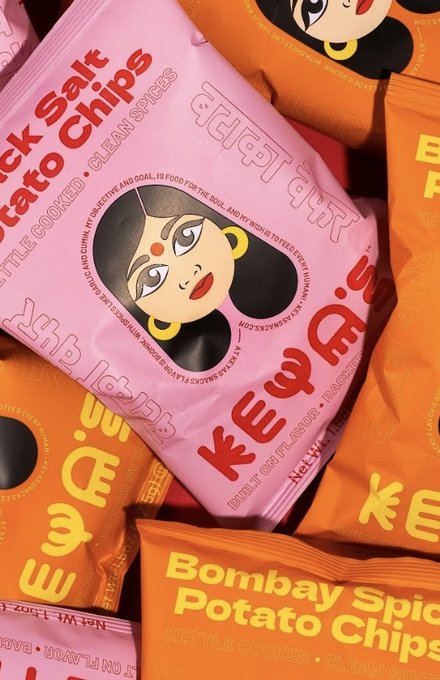 A pile of Keya's Black Salt and Bombay Spice potato chip bags in pink and orange, each with an illustrated woman's face