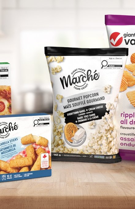 Grocery private brand packs on a kitchen counter: Only Goodness cauliflower crust pizza, Marche gourmet popcorn and Plant Value rippled chips and mac & cheese